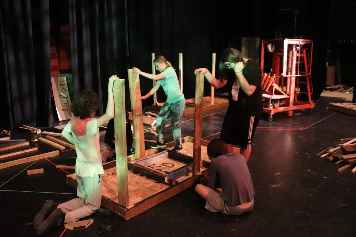 Members of the set crew work on drilling the legs onto a flat during a tech work session.
